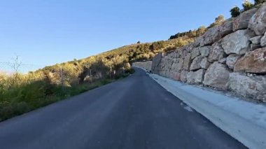 Etrafı yemyeşil tepeler ve kayalık arazilerle çevrili çarpıcı ve dolambaçlı bir yolun görüntüsü.