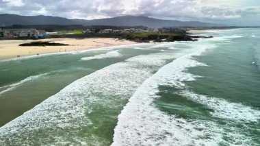 Yatıştırıcı sahil dalgalarının, kumlu kıyıların ve arka planda yemyeşil tepelerin güzel hava görüntüleri..