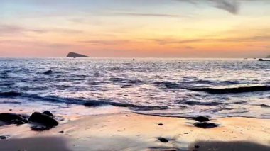 Gün batımında güzel ve sakin bir sahil sahnesi. Yumuşak dalgalar sergileniyor. Kayalık bir sahil şeridinde rahatlamak için mükemmel.