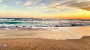 Nazik dalgaların sakin bir sahnesiyle baş döndürücü ve renkli bir günbatımında altın sahili hafifçe okşayarak