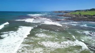 Bir hava görüntüsü okyanus dalgalarının engebeli bir kıyı şeridine çarpıp açık mavi gökyüzünün altında güzelliği yaratmasını sağlar.
