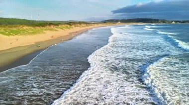 Zarif dalgaların altın kumu yalayıp yuttuğu ve gerçekten sakin bir atmosfer oluşturduğu çarpıcı ve güzel bir sahil sahnesi.