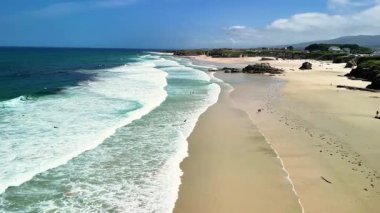Bu manzaralı sahil manzarasında yumuşak dalgalar ve berrak mavi gökyüzü var. Rahatlamak ve doğal güzellikler için mükemmel.