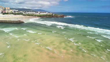 Hava görüntüsü, mavi gökyüzünün altındaki kumlu sahillere çarpan canlı dalgaları yakalıyor. Macera ve sükuneti çağrıştırıyor.