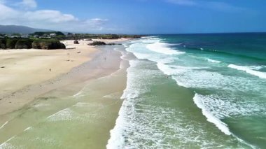 Bu nefes kesici dron görüntüsü güneşli bir günde sakin dalgaları yavaşça kumlu kumsalda yakalar.