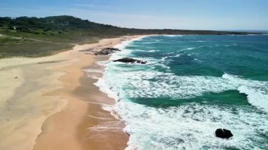 Yumuşak dalgalar ve etrafını saran yemyeşil tepelerle sakin bir plajın nefes kesici manzarasının tadını çıkar.