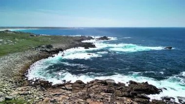 Okyanus dalgalarının nefes kesen görüntüsü berrak mavi gökyüzünün altında kayalık kıyılara çarpıyor.