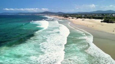Zarif dalgaların ve açık mavi gökyüzünün bulunduğu nefes kesici ve resimli bir sahilin havadan görünüşü.