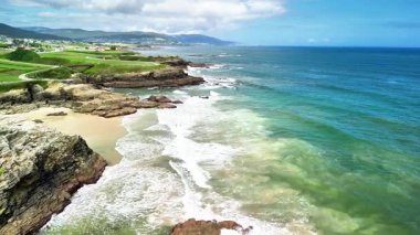 Sahilde dalgalar, engebeli kayalar ve yemyeşil manzaralarla güzel kıyı manzarasının tadını çıkarıyorum.