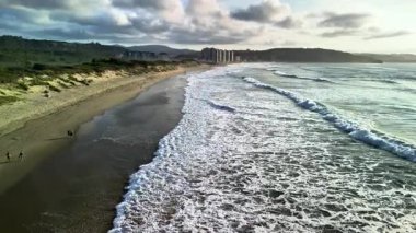 Büyüleyici bir sahil sahnesi güzel dalgalar ve günbatımında geniş bir kıyı manzarası sergiliyor.
