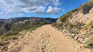 Göz kamaştırıcı bir kumlu patika, parlak mavi gökyüzünün altındaki muhteşem kayalık dağlarda güzel bir şekilde süzülür.