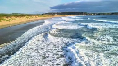 Okyanus dalgalarının büyüleyici görüntüsü kıyıya güçlü bir şekilde çarpıyor, güzel, sakin bir sahil manzarası sergiliyor.