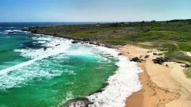 Nefes kesici bir hava manzarası, kristal berrak turkuaz sular ve kayalık bir kıyı şeridinin yer aldığı çarpıcı bir sahili gösteriyor.