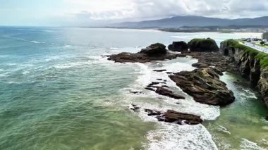 Okyanus kıyısındaki sarp kayalıkların çarpıcı manzarası güzelliği ve kıyı şeridini kaplayan nazik dalgaları vurguluyor.