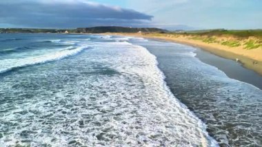 Büyüleyici hava manzarası, yumuşak okyanus dalgalarının güzel kumlu bir sahile ritmik bir şekilde çarptığını gösteriyor.