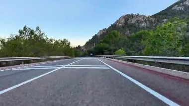 Nefes kesici bir dağ manzarasında, parlak ağaçlar ve açık mavi gökyüzü olan güzel, dolambaçlı bir yol.