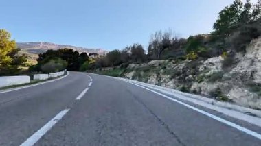 Arka planda yemyeşil ve görkemli tepelerin sardığı dolambaçlı bir yolun nefes kesici manzarası.