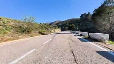 Parlak mavi bir gökyüzünün altında uzanan dolambaçlı bir dağ yolunun nefes kesici manzarası, seyahat görüntüleri için ideal.