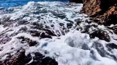 Bu güzel sahil sahnesinde canlı, renkli kaya havuzları ve köpüklü köpükler oluşturan yumuşak okyanus dalgaları sergileniyor.