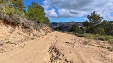 Engebeli, dolambaçlı bir toprak yol, temiz, mavi gökyüzü ile süslenmiş, görkemli dağlık bir arazide yılan gibi yol alır.
