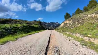 Göz kamaştırıcı ve güzel çakıllı bir yol Görkemli dağların arasından kıvrılıyor ve berrak mavi gökyüzünün altında yemyeşil.