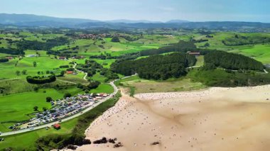 Göz kamaştırıcı bir hava görüntüsü, yemyeşil tepelerin arasına yerleştirilmiş sakin bir kumsalın güzelliğini yakalar.