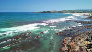 Uçsuz bucaksız okyanus, el değmemiş plaj ve güneşli gökyüzünün altındaki engebeli sahil manzarası.