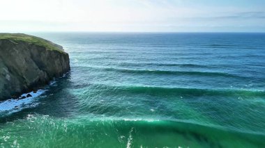 Dalgalanan okyanus dalgalarının ve yemyeşil kayalıkların huzur veren güzelliğine dalın bu çarpıcı sahil manzarasında.