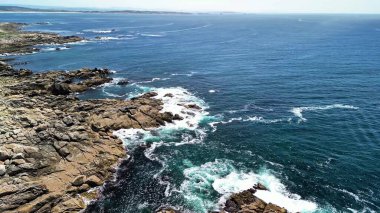 Canlı mavi okyanus dalgalarıyla kusursuz bir şekilde harmanlanan kayalık kıyıların nefes kesici hava manzarasını deneyimleyin.