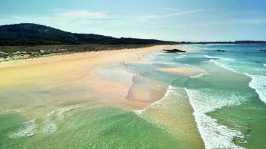 Yumuşak dalgaları, altın kumları ve berrak mavi gökyüzü olan sakin bir plajın tadını çıkarın.