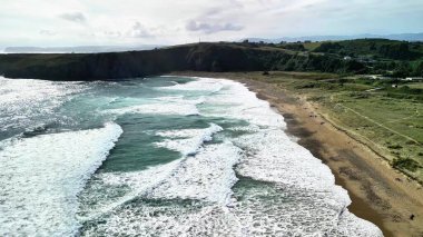 Sakin bir plajın çarpan dalgaları ve yemyeşil bir sahil şeridinin çarpıcı hava görüntülerini tecrübe edin.