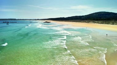 Huzurlu ve sakin bir sahil manzarası berrak suları, yumuşak dalgaları ve uzak bir kıyı şeridini sergiler.
