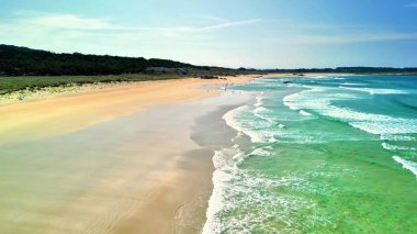Berrak mavi sular, yumuşak altın kum ve yumuşak dalgaların sergilendiği şaşırtıcı derecede güzel bir sahil manzarası.