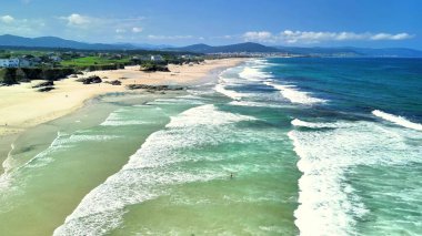 Parlak güneş ışığı altında dalgaların yavaşça kıyıya vurduğu güzel bir sahilin nefes kesici manzarasının tadını çıkarın.
