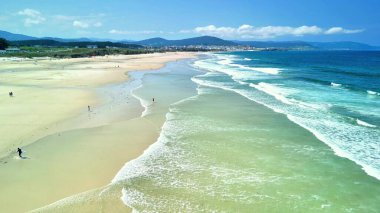 Yumuşak dalgaları ve berrak mavi gökyüzünün altında huzurlu bir atmosferi sunan çarpıcı bir sahil sahnesi.