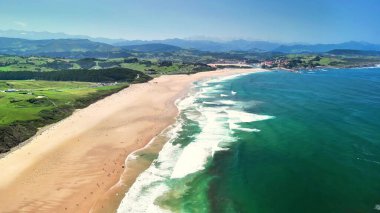 Nefes kesici bir kıyı manzarası çarpıcı bir kumsal ve dalgalı dalgalar altında berrak ve parlak mavi bir gökyüzü