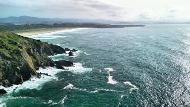 Bu çarpıcı manzara sarp okyanus kayalıklarını gösteriyor. Dalgalar bulutlu bir gökyüzünün altında kayalık kıyılara çarpıyor.