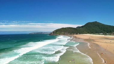 Arkasında dalgalar ve yemyeşil tepeler olan canlı bir tropikal plajın çarpıcı manzarası.