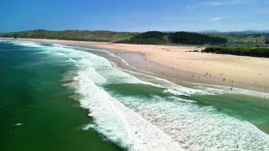 Dalgaların açık gökyüzünün altındaki yumuşak kumlu kıyılara çarptığı nefes kesici bir sahilin geniş bir hava manzarası.