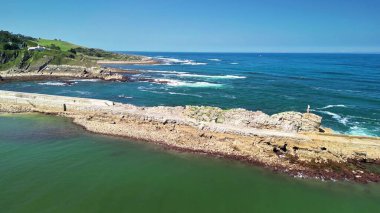 Kayalık kıyıları, berrak suları ve parlak mavi gökyüzünün altında hafif dalgaları olan çarpıcı bir kıyı manzarası.
