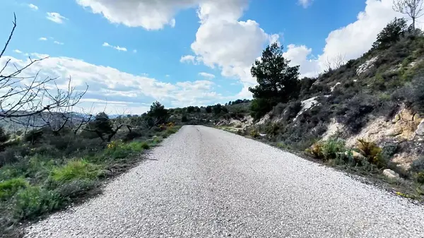 Güzel bir çakıl yolu bulutlarla dolu mavi bir gökyüzünün altında, pitoresk manzaralar arasında yol alır.