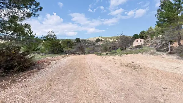Sakin bir toprak yol, berrak mavi gökyüzü altında canlı yeşillikler ve çarpıcı doğal güzellikler arasında zarif bir şekilde esiyor.