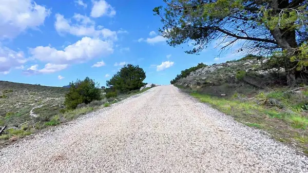 Güzel, manzaralı çakıllı bir yol, parlak, yemyeşil ve kayalık bir arazide, berrak mavi gökyüzünün altında yol alır.