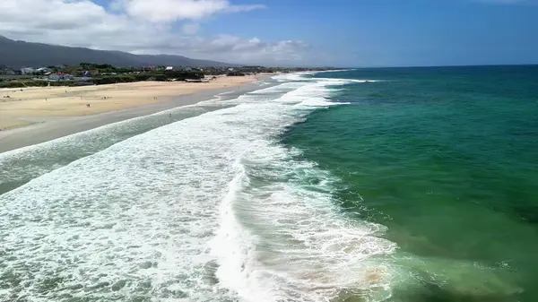Hafif dalgaların huzur veren güzelliğini keşfetmek için bir dakikanızı ayırın. Güneşli bir sahilde ritmik bir şekilde kıyıya çarpan dalgaların.