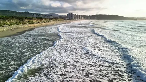 Sahile vuran güzel sahil dalgaları, gün batımında arka planda binalar ve tepeler.