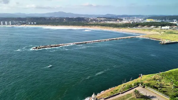 Hava manzarası, açık mavi gökyüzünün altında uzun bir iskele ve nazik dalgalarla güzel bir kıyı şeridini gözler önüne serer.