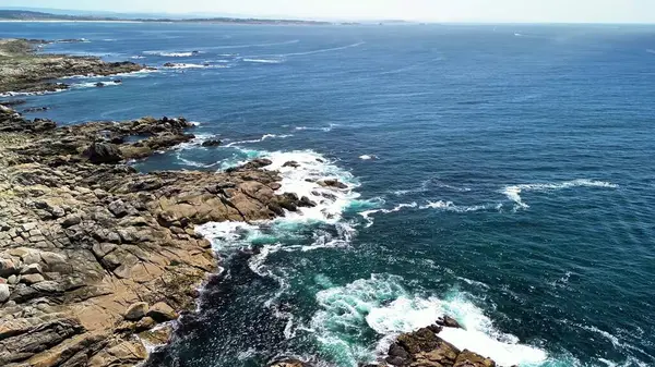 Canlı mavi okyanus dalgalarıyla kusursuz bir şekilde harmanlanan kayalık kıyıların nefes kesici hava manzarasını deneyimleyin.