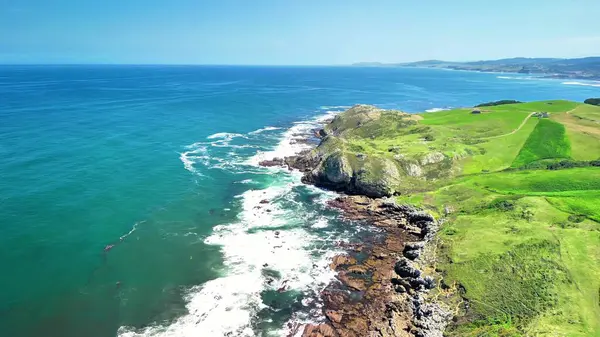 Güçlü dalgaların kayalara çarptığı canlı bir kıyı manzarasını gösteren nefes kesici bir hava manzarası yaşayın.