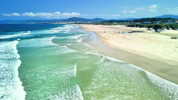 Bir hava fotoğrafı, kıyı şeridi boyunca berrak turkuaz suları ve yumuşak altın kumları olan sakin bir sahili yakalar.