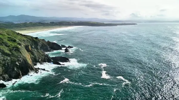 Bu çarpıcı manzara sarp okyanus kayalıklarını gösteriyor. Dalgalar bulutlu bir gökyüzünün altında kayalık kıyılara çarpıyor.